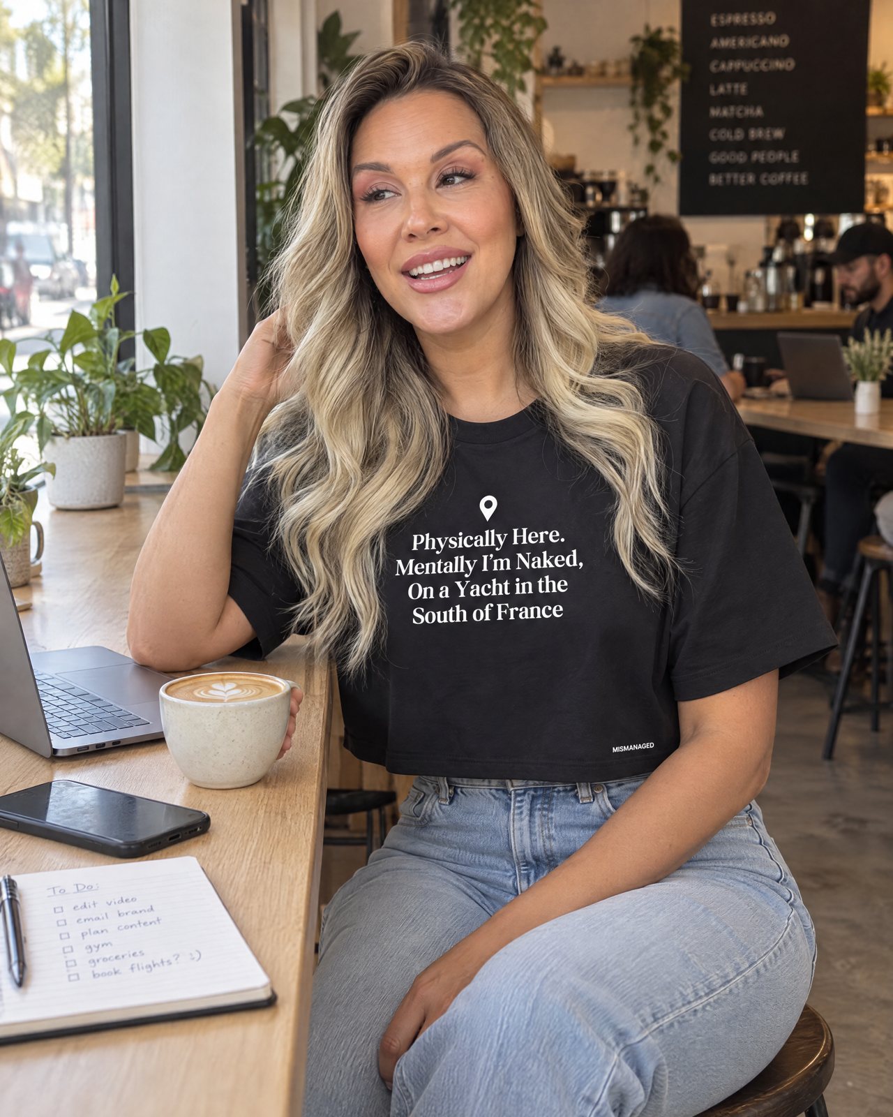 Model wearing the South of France crop tee, front view, in a coffee shop, lifestyle view